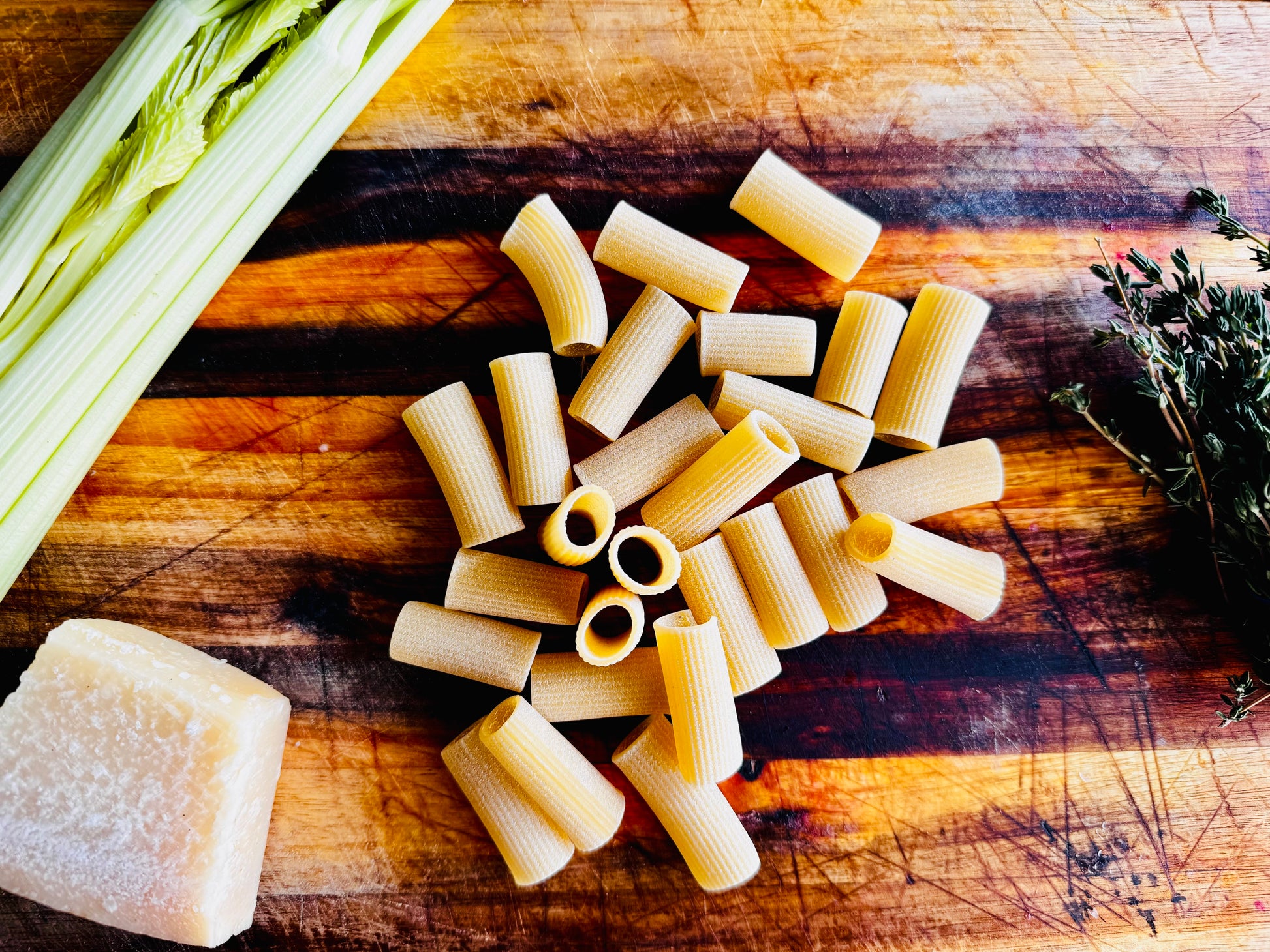 Flayvr Cooking Kit with Rigatoni Pasta, Fresh Celery, Thyme, and Parmesan Cheese on Wooden Cutting Board
