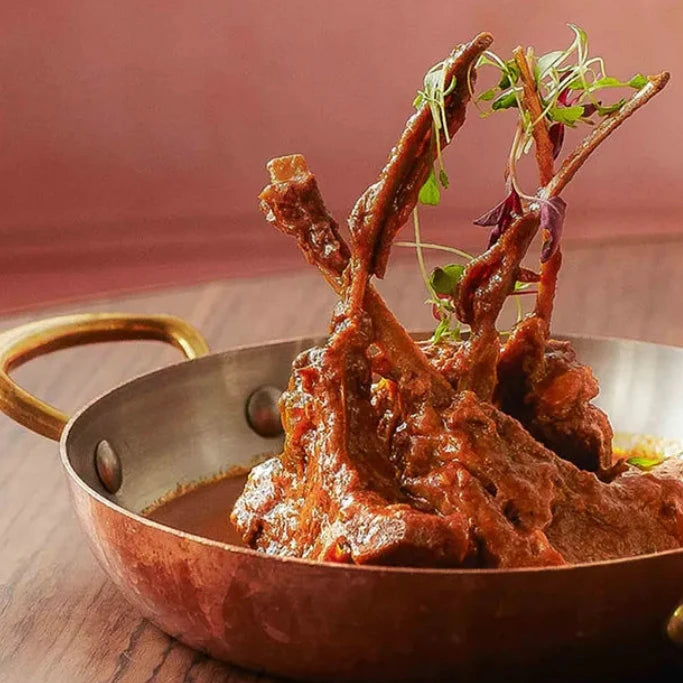 Copper pan with roasted lamb dish on a wooden table