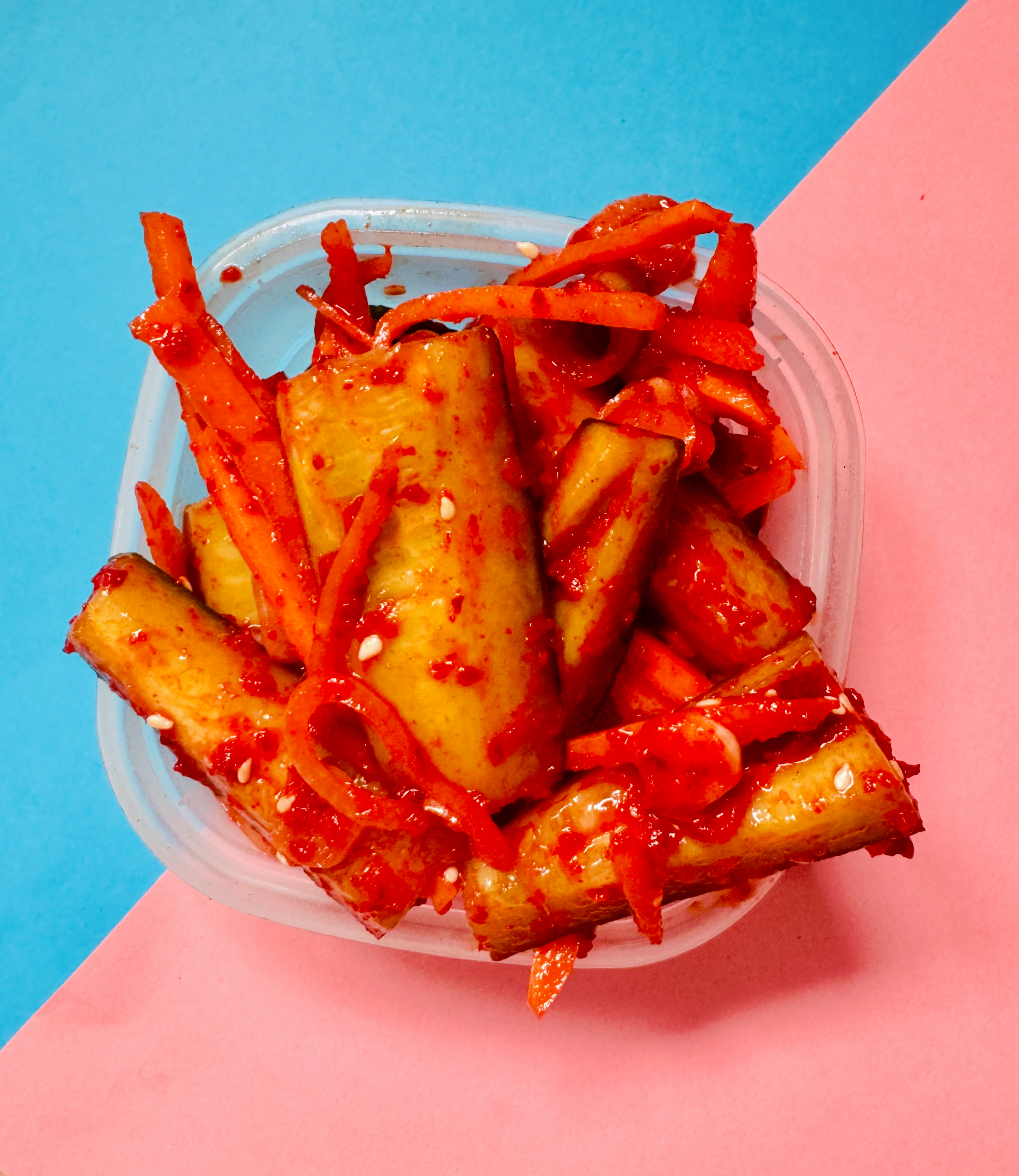 Crunchy cucumber kimchi in a clear container with vibrant red chili and vegetables