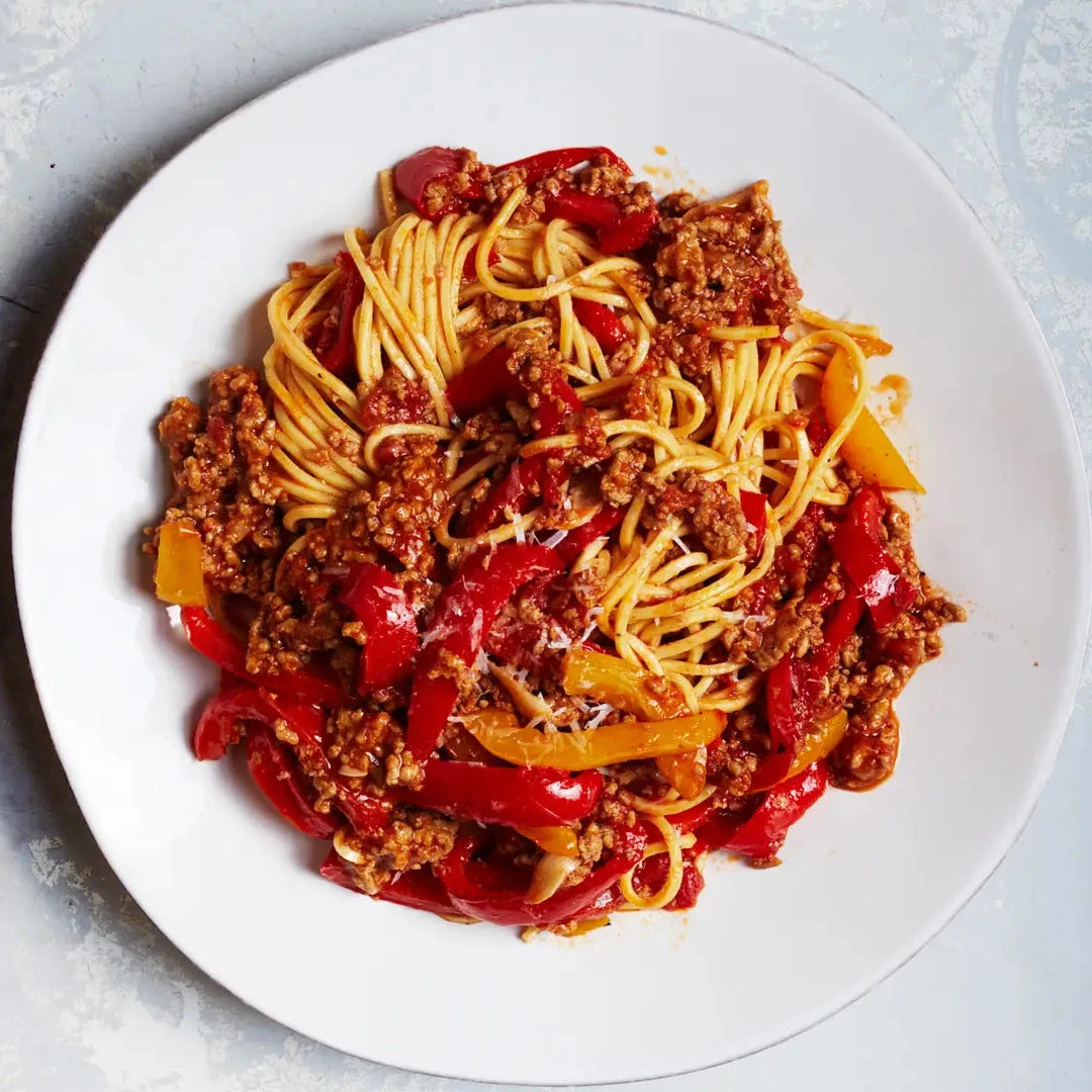 Spaghetti dish with meat sauce on a white plate against a light gray background